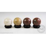 Four stone spheres of polished marble and agate, each on a turned and carved ebonised stand, each