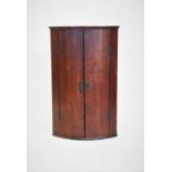 A George III oak bow front hanging corner cupboard, the two doors enclosing two shelves, 93cm high