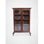 An early 20th century glazed oak bookcase, with two glazed doors and three shelves, raised upon