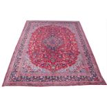 A large red ground Persian Mashad carpet with a traditional medallion design, 390cm x 300cm