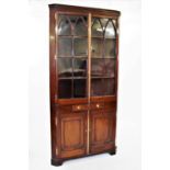 An early 19th century mahogany freestanding corner cupboard, with a moulded cornice above a pair