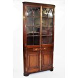 An early 19th century mahogany freestanding corner cupboard, with a moulded cornice above a pair