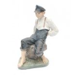 Royal CopenhagenA porcelain figure of a shepherd boy with whip seated on a stone, design Christian