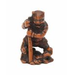 A boxwood netsuke, Oni holding a staff with characters, dressed in animal hides, three human figures