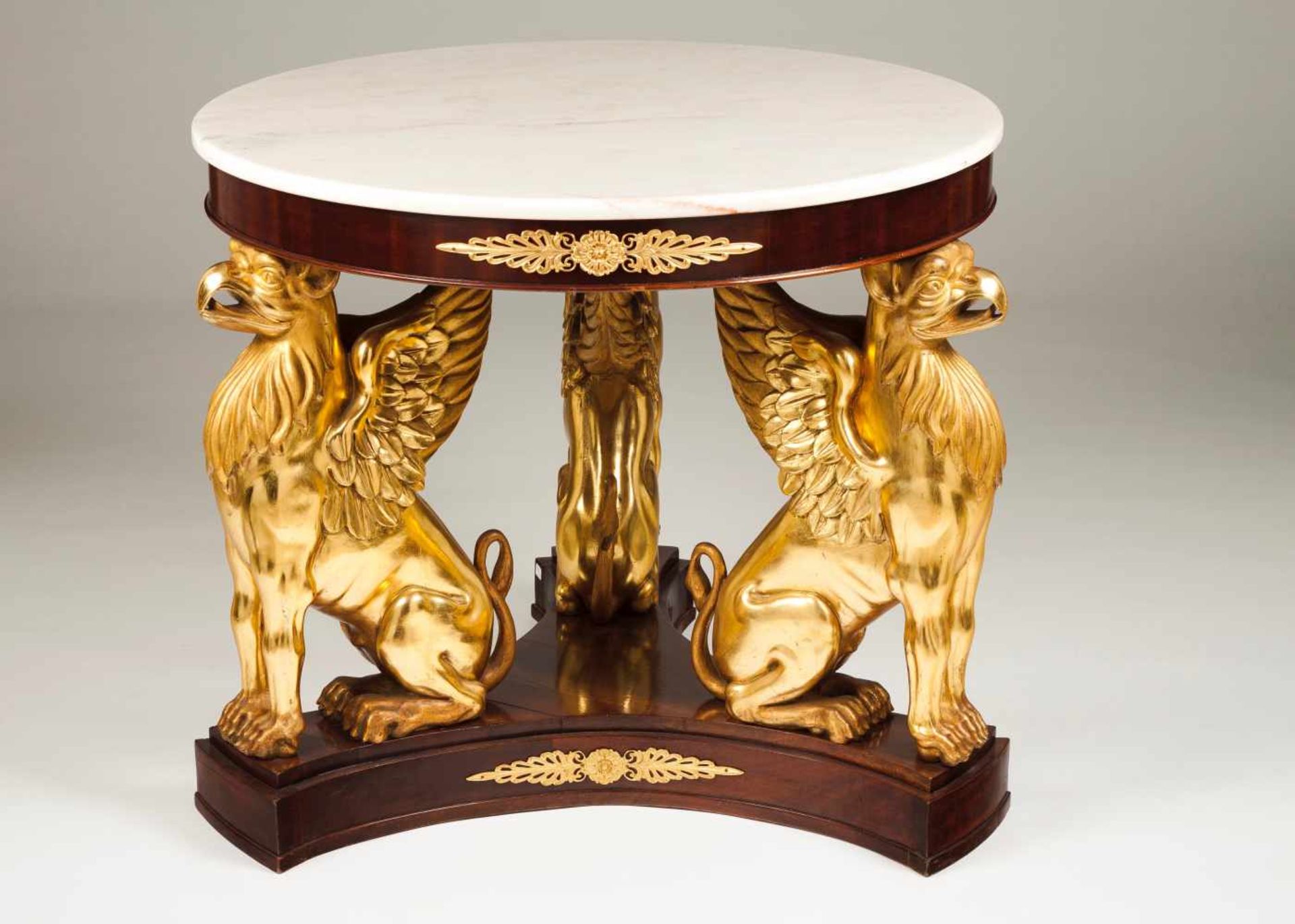 An Empire style centre tableMahogany veneered woodCarved and gilt decoration Griffin-shaped legs,