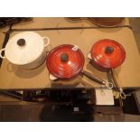 Two red Le Creuset pans with lids and one white twin handled pan