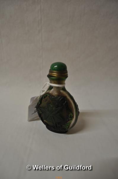 A Chinese glass snuff bottle, green cabochon stone to lid, carved with bats and leaves, 7cm.