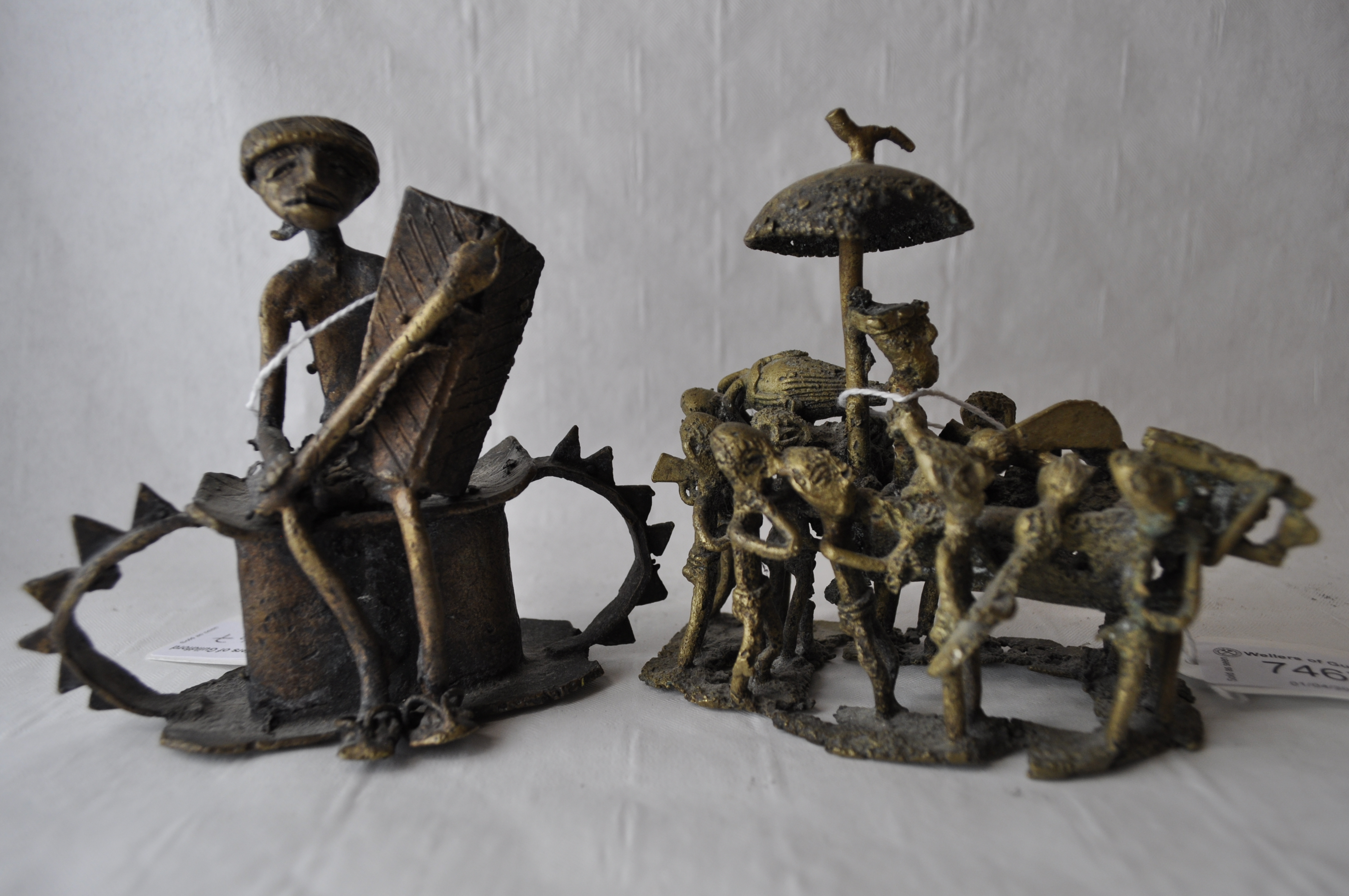 A naive African bronze figure group of a group of men carrying a chieftain, separate wooden stand,