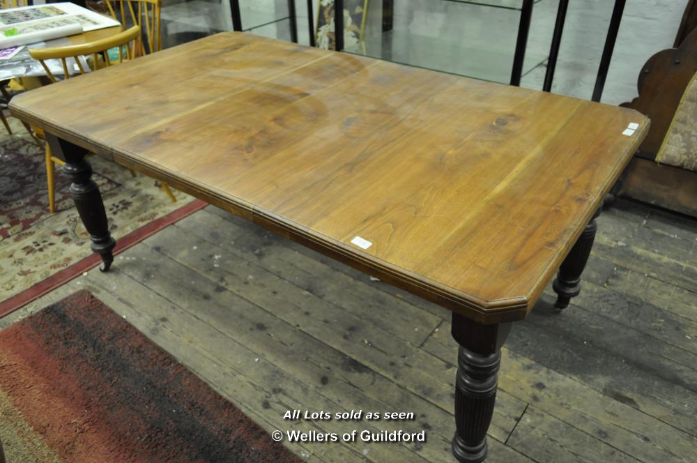 An Edwardian walnut extending dining table with canted corners, one extra leaf and winding handle,