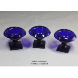 Three blue glass salts with rolled rims, each 7cm high.
