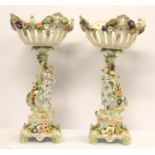 A pair of Continental porcelain comports with pierced bowls, figural supports, applied floral