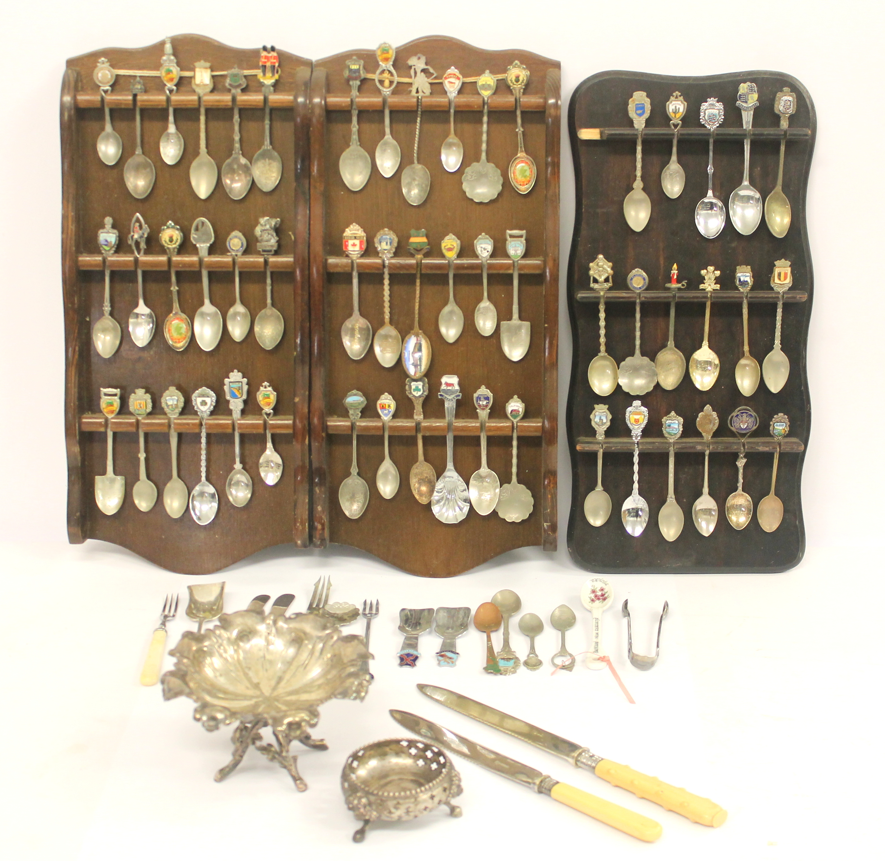A quantity of silver plated souvenir spoons with three wooden display racks; white metal pierced