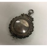 A circular silver fob attractively decorated with