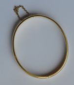 A gold hinged bangle with safety chain. Approx. 12