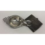 A stylish silver tea strainer together with an eng