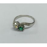 An emerald and diamond two stone crossover ring in