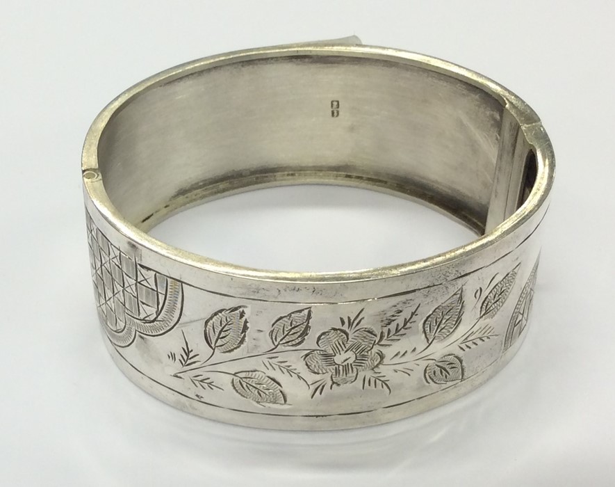 A hinged silver bangle with leaf decoration and co