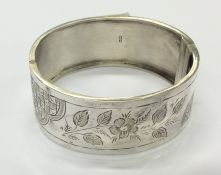 A hinged silver bangle with leaf decoration and co