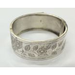 A hinged silver bangle with leaf decoration and co