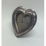 A silver heart shaped picture frame clock with sil