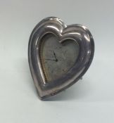 A silver heart shaped picture frame clock with sil