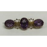 An amethyst three stone gold brooch in claw mount.