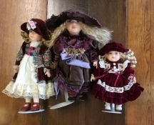 Three dressed porcelain headed dolls in crimson an