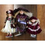 Three dressed porcelain headed dolls in crimson an