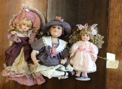 Three dressed porcelain headed dolls in pink and l