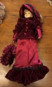 A dressed porcelain headed doll in crimson gown. E