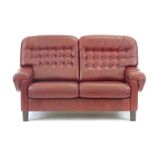 A 1970's burgundy button upholstered two seater armchair on square feet,