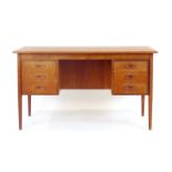 A 1970's Danish teak and crossbanded desk with an arrangement of six drawers on circular tapering