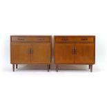 A pair of 1970's teak cabinets, each with a single drawer and two doors on turned legs, w.