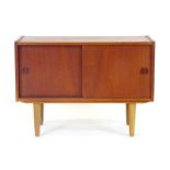 A 1970's Danish teak cabinet with two sliding doors and integral handles on later turned legs, w.