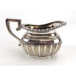 An Edwardian silver and parcel gilt cream jug of squat urn shaped form with gadrooned decoration,