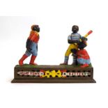 A cast iron money box in the form of three baseball players, 'Hometown Battery', w.