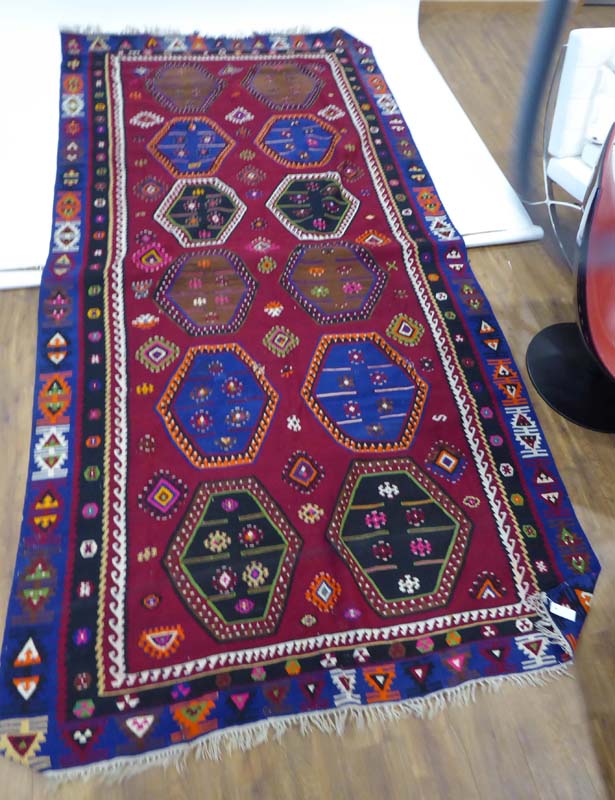 A hand woven Kelim carpet decorated with hexagonal motifs in various shades on a claret ground,