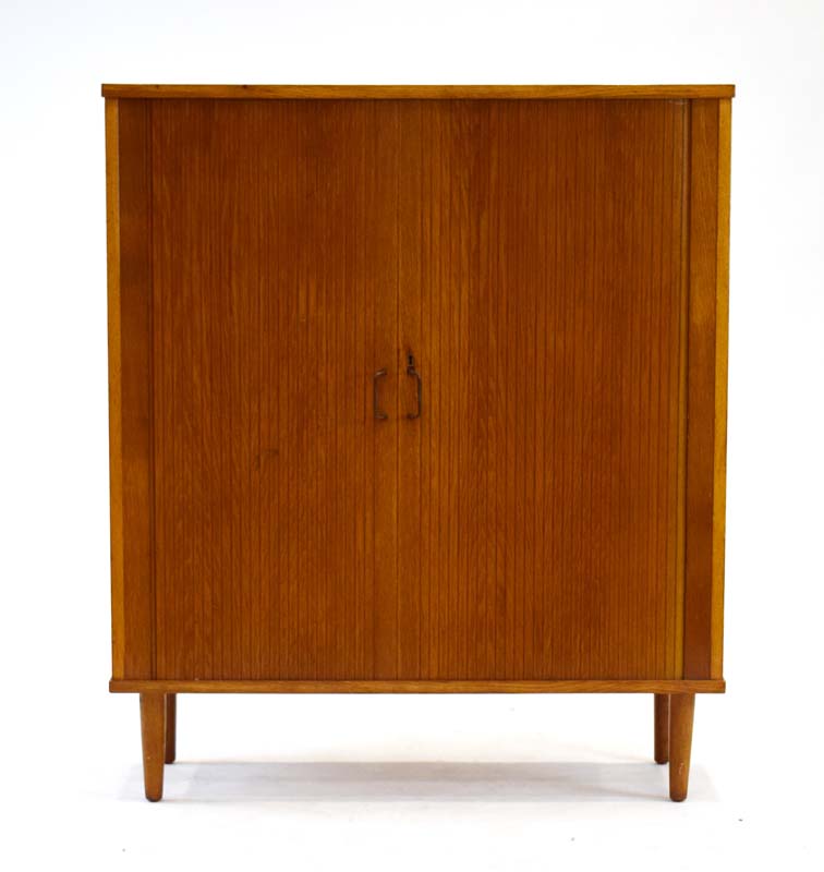 A 1960's oak and crossbanded cabinet, the tambour doors enclosing nine drawers, on turned legs, w.