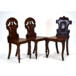 A pair of Victorian mahogany hall chairs with armorial backs over solid seats,