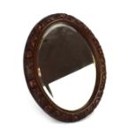 LATE ENTRY: A late 19th/early 20th century wall mirror of oval form within a walnut frame carved