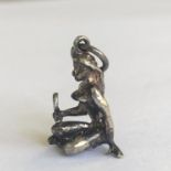 A vintage silver metal charm depicting a nude woman