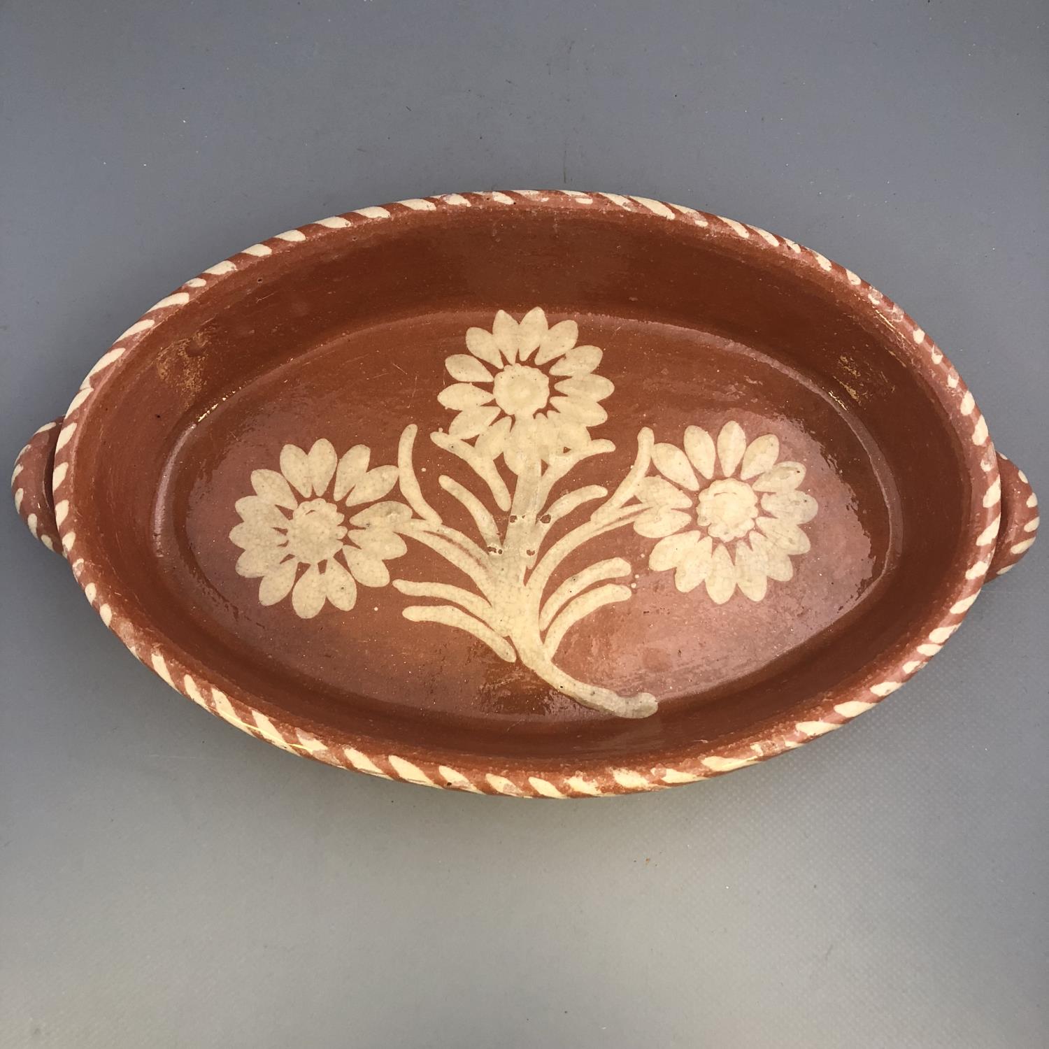 A twin handled slipware pottery dish of oval form with floral decoration