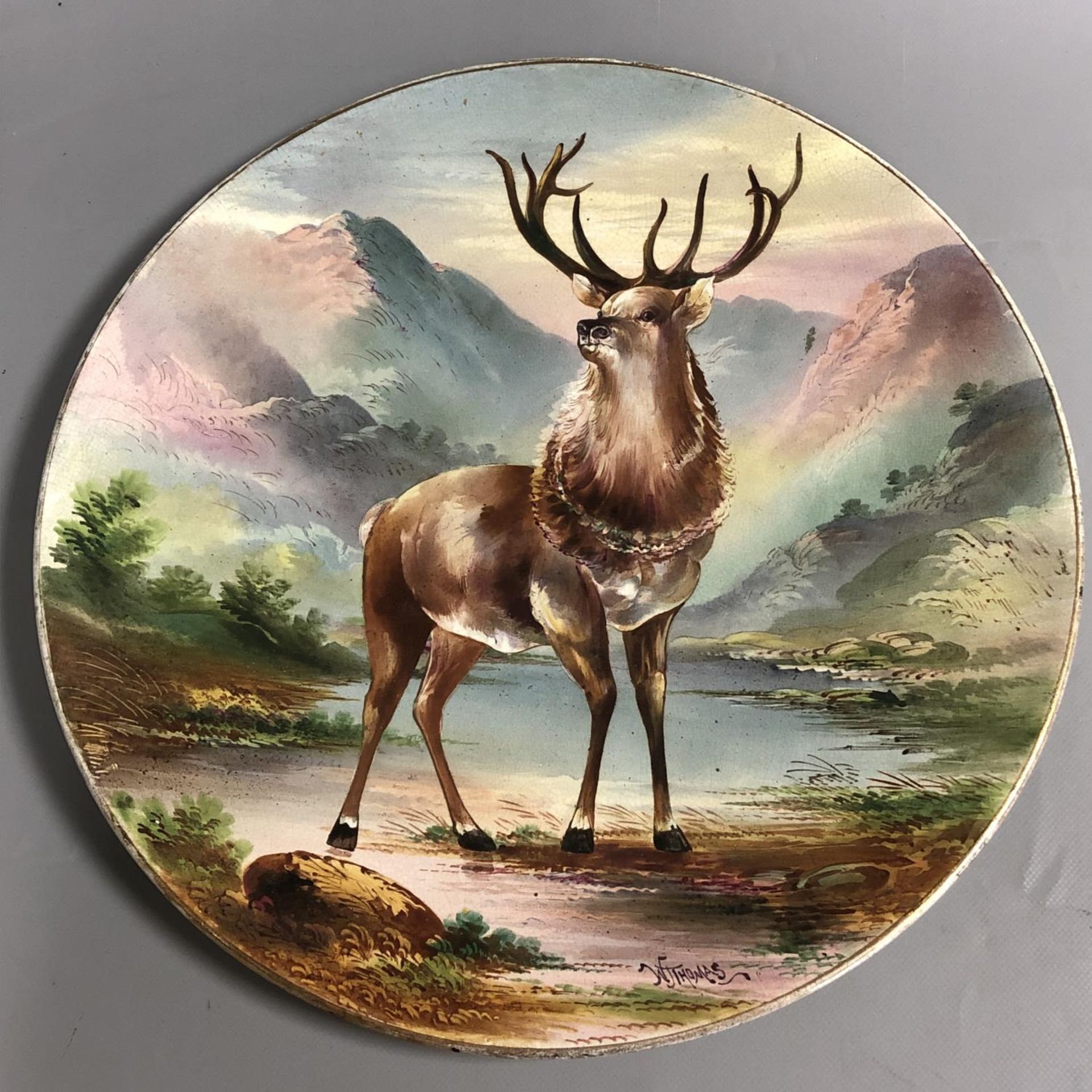 A large antique circular pottery plaque with hand painted scene of a Highland Stag. Signed W Thomas.