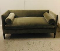 A Large sage green velvet sofa with bolster cushions.