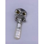 A silver babies rattle in the form of an owl with glass eyes with M O P handle