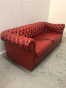 A Two seater Chesterfield sofa in a burnt orange colour.
