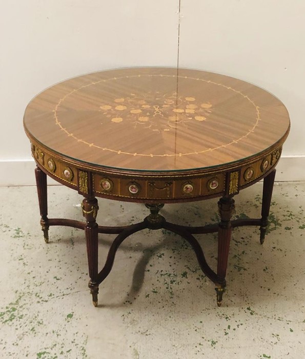 A Round Ornate centre table with marquetry top with glass overlay, curved x stretcher on six legs