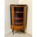 An Ornate corner cabinet with brass detailing, marquetry and a curved glass door and three shelves.
