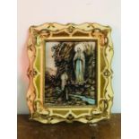 A Religious picture in a cream and gilt frame with a light behind.