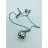 A silver necklace with a cage ball pendant
